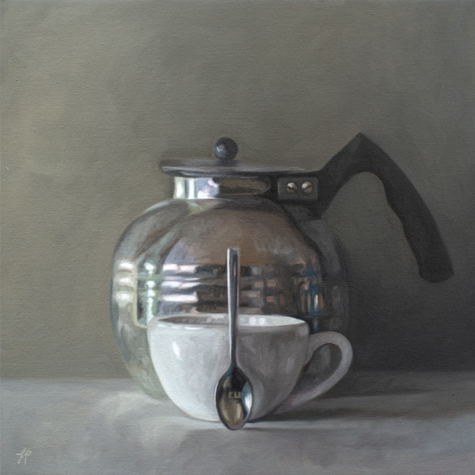 A vintage tea kettle, porcelain cup and spoon rest on a grey surface with a dark and moody background.
