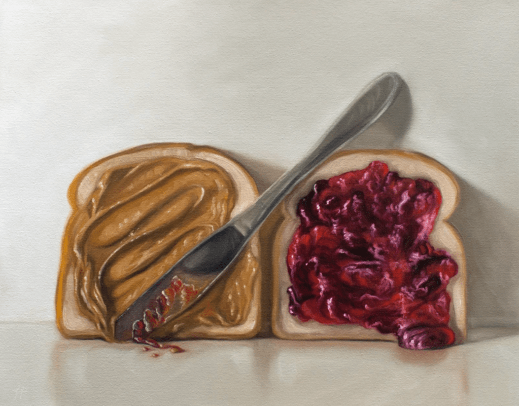 A peanut butter and jelly sandwich in-the-making rests on a light, reflective surface with the addition of a diagonally placed butter knife.